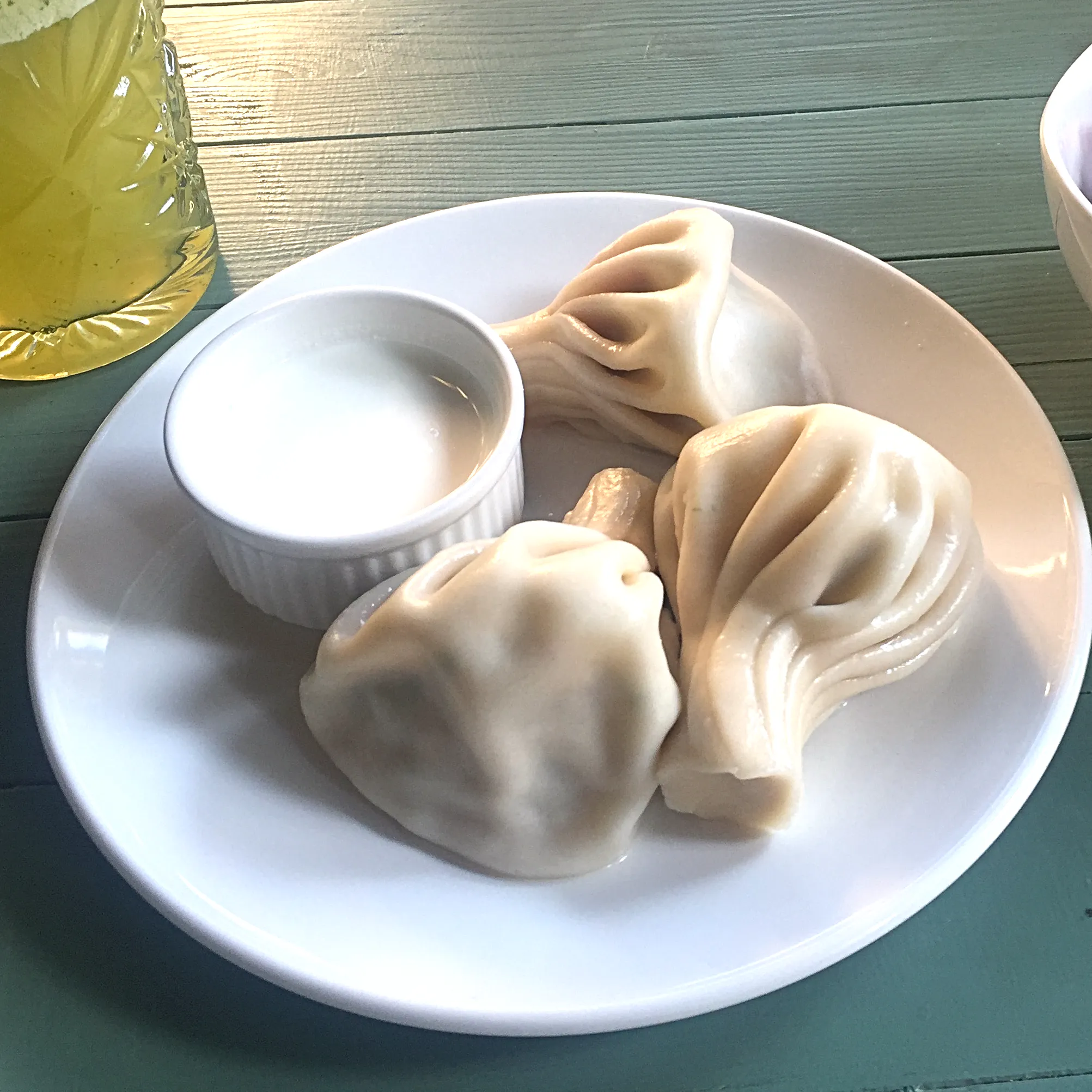 Tre kokta chinkali med veckade degknutar på en vit tallrik tillsammans med en liten skål vit vitlöksgräddfil.