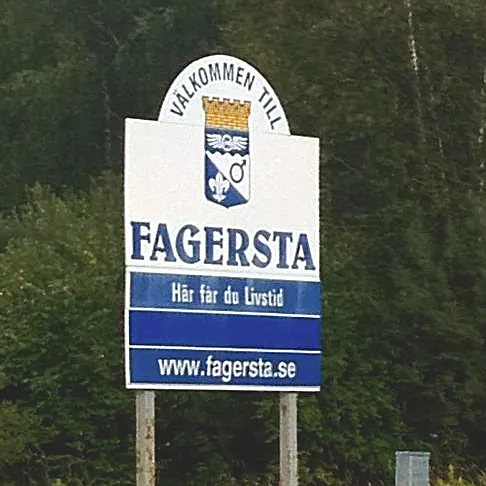 Vita och gula blommor ligger på blöt grå asfalt intill en kantsten, med ett släckt ljus i en glasburk vid sidan.