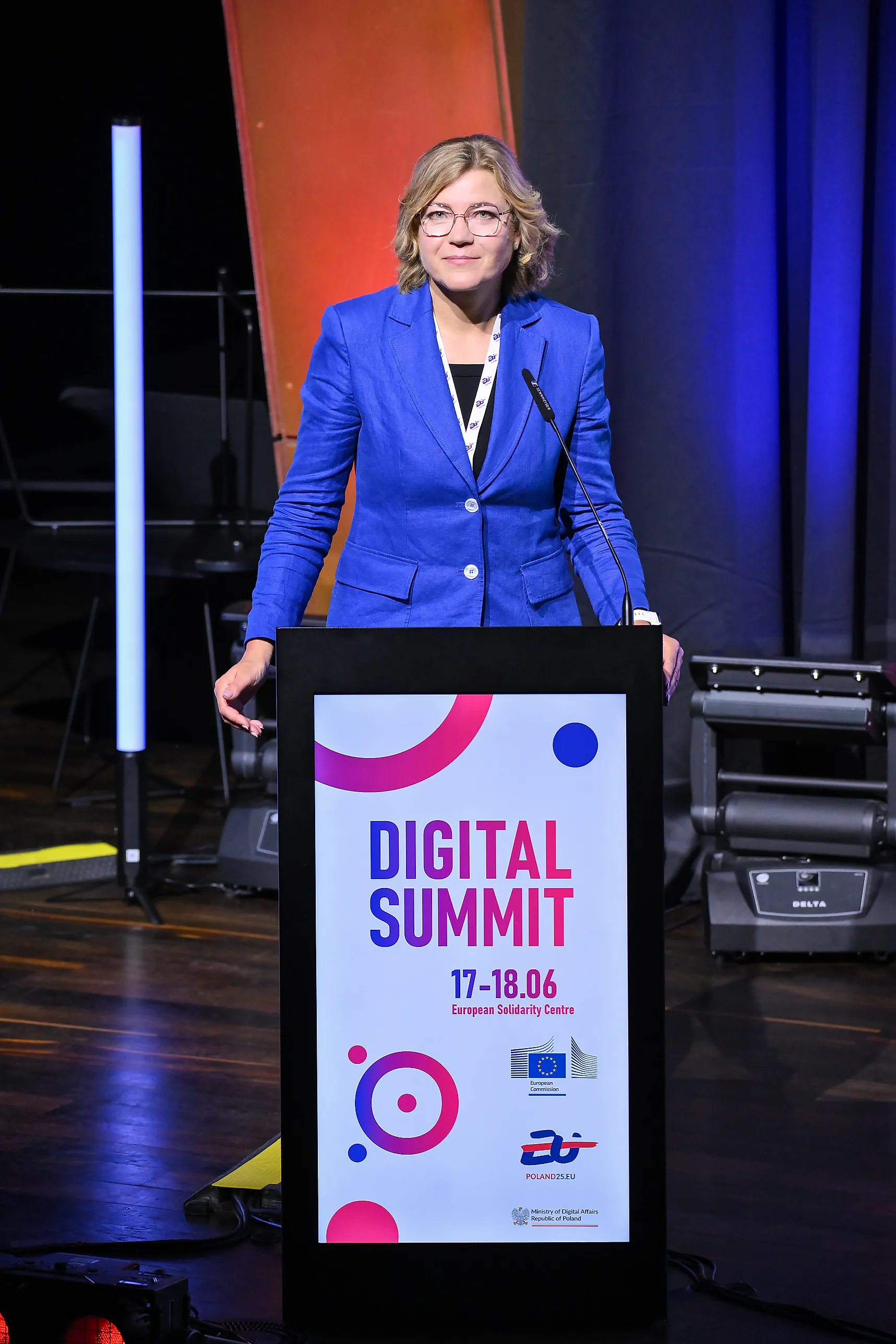 Henna Virkkunen i klarblå kavaj står vid ett talarpodium med texten "Digital Summit 17–18.06" och EU-kommissionens logotyp på en scen.