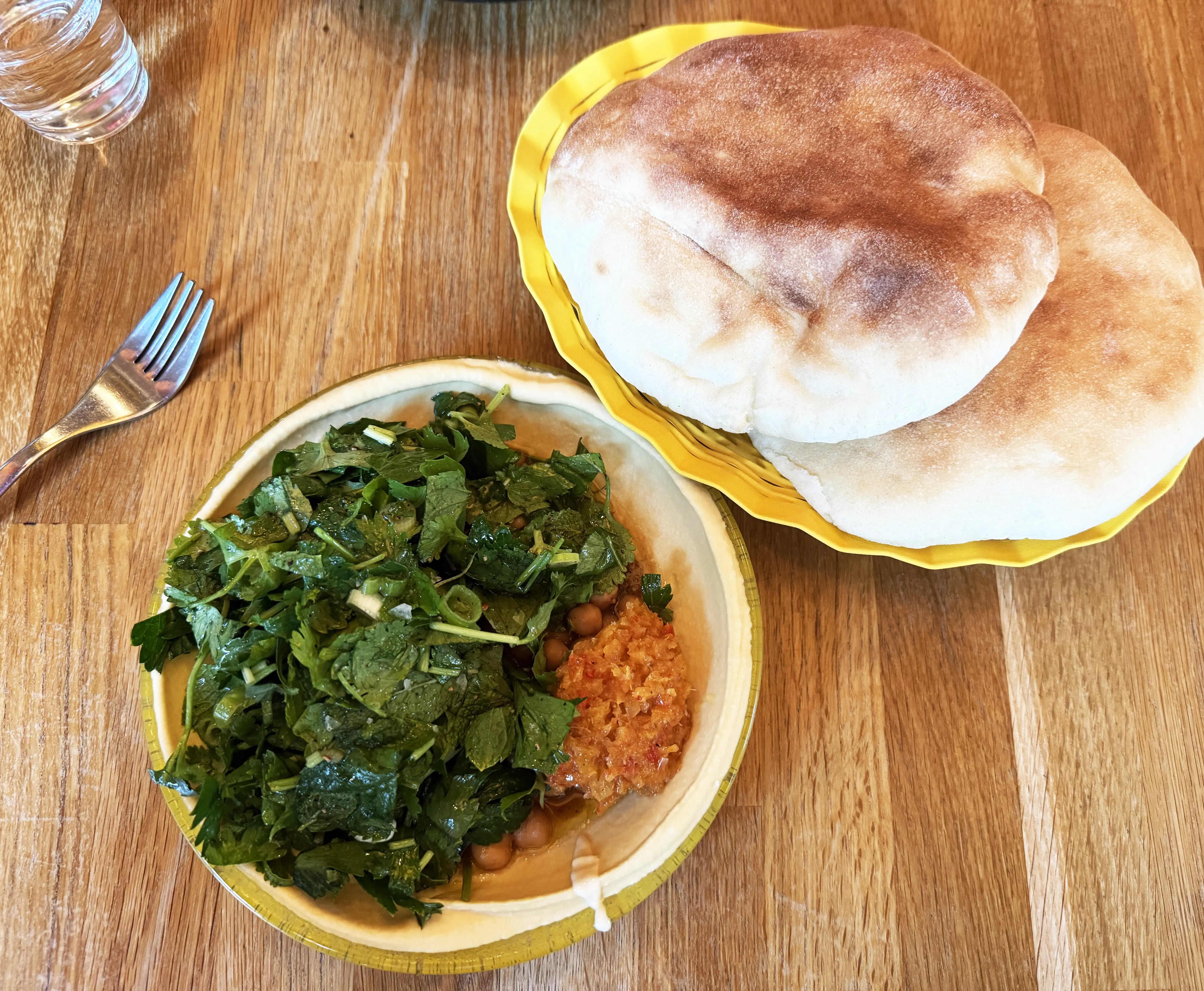 Skål med hummus toppad med örtsallad, kikärtor och harissa, bredvid två nygräddade pitabröd