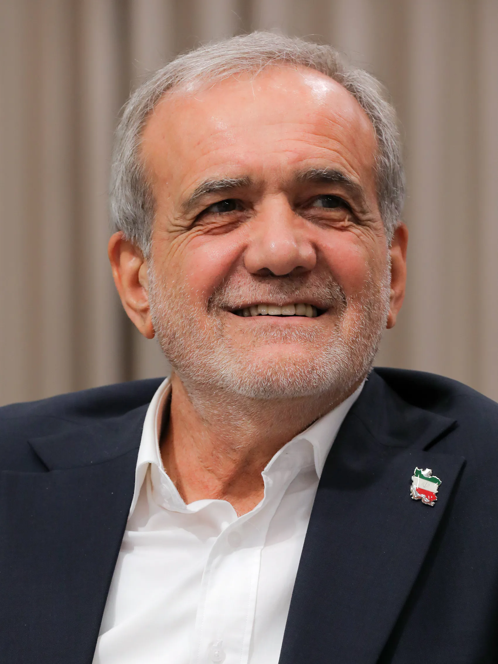 Irans president Masoud Pezeshkian ler och tittar åt sidan, i vit skjorta och mörk kavaj med en nål i form av Iran i flaggans färger på slaget.