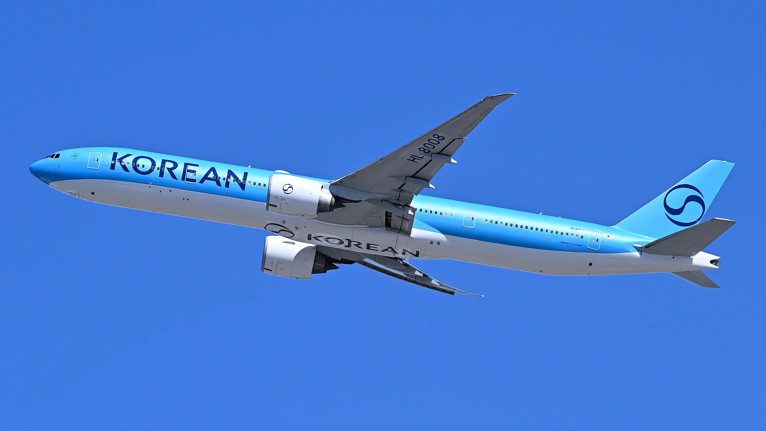 Ljusblått och vitt Korean Air-plan med utfällda landningsställ stiger mot klarblå himmel.