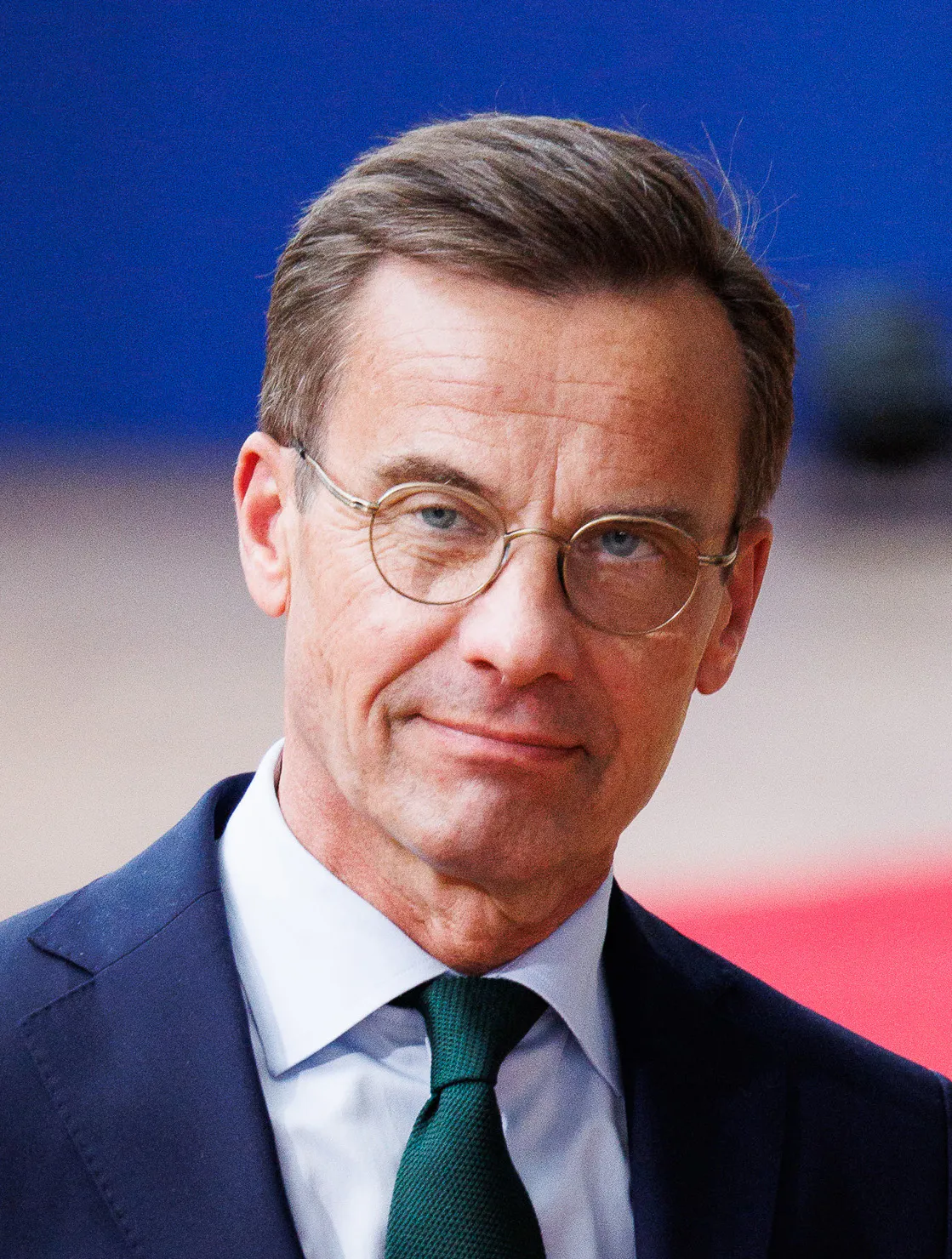 Ulf Kristersson i mörk kostym, vit skjorta och grön slips, med runda glasögon.