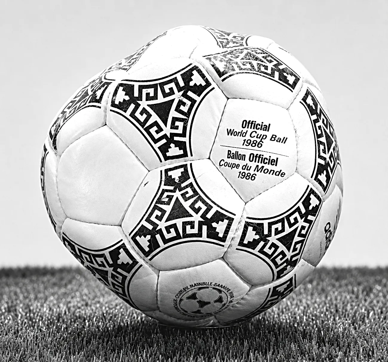 En gammal, nött fotboll ligger på mörk sammet i ett glasskåp, svagt uppifrånljus.