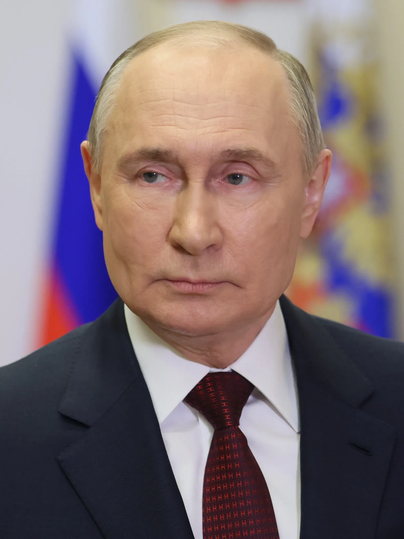 Vladimir Putin i mörk kostym och röd slips framför den ryska flaggan.