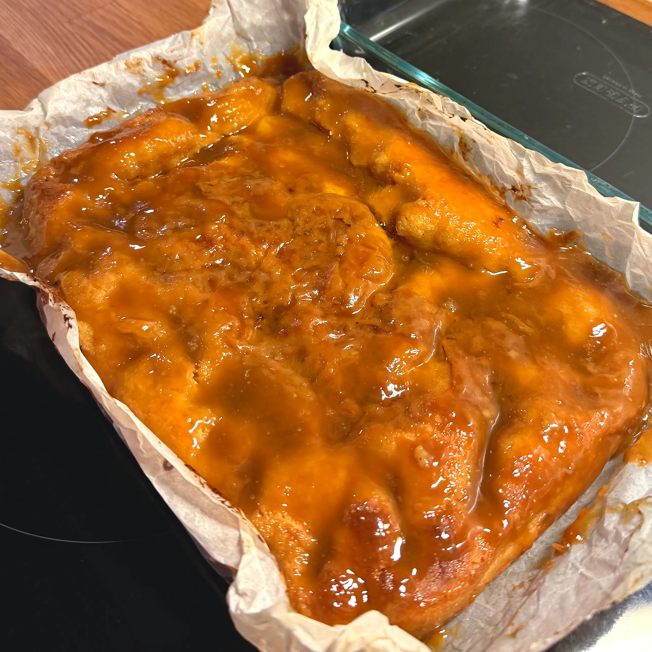 Nybakad rektangulär jästkaka på bakplåtspapper i en glasform, täckt av en blank, bubblande karamell av smör och farinsocker.