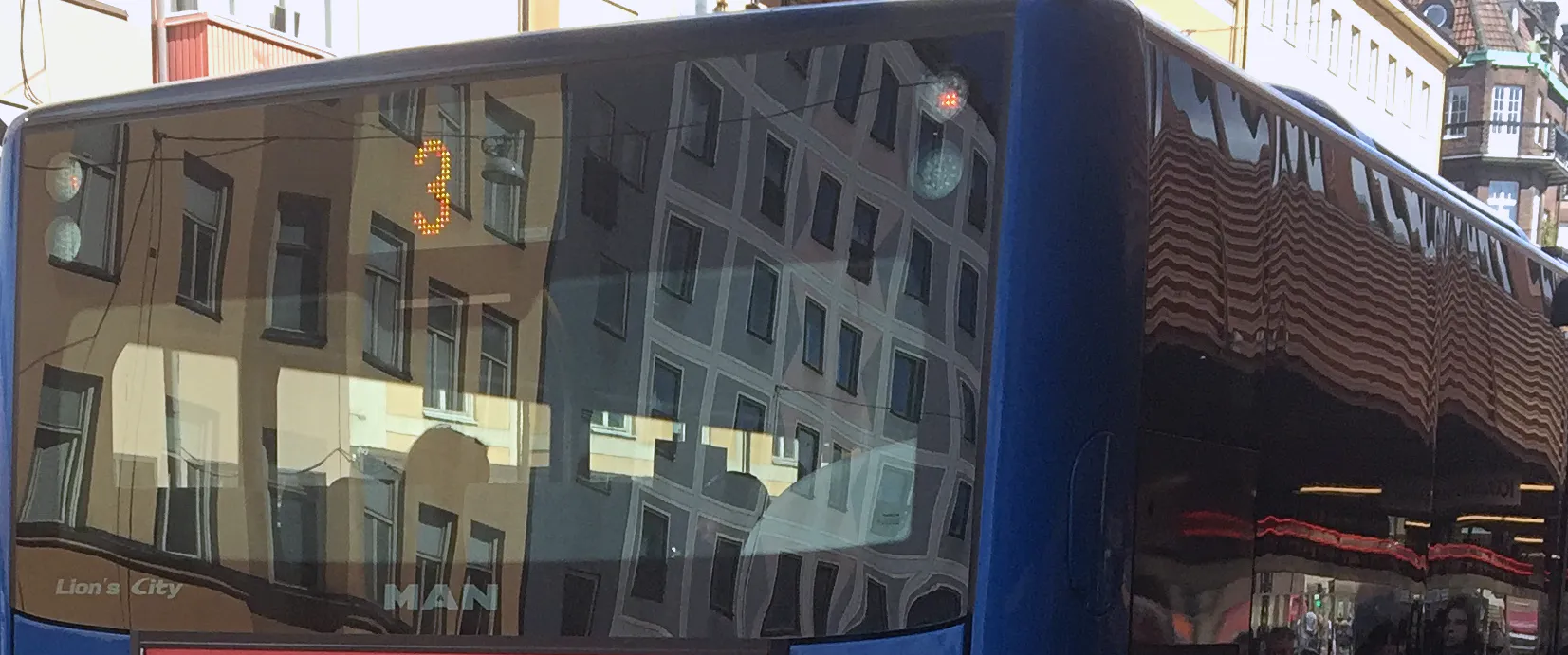 Rader av tomma bussäten med mönstrat blågrått tyg och kromade stänger, varmt ljus genom sidofönstren.