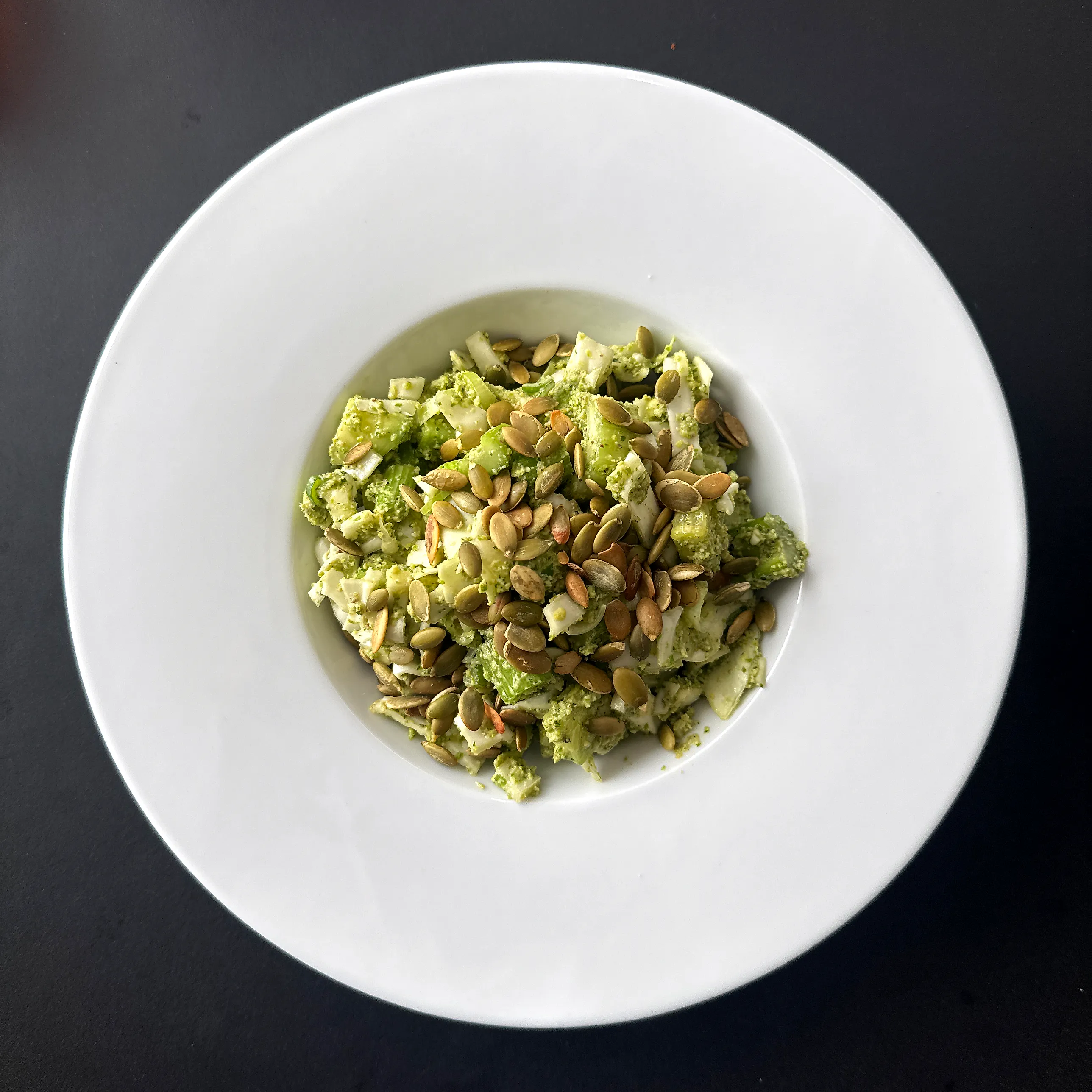 Djup vit tallrik med finhackad grön sallad täckt av krämig grön dressing och ett generöst lager rostade pumpafrön.