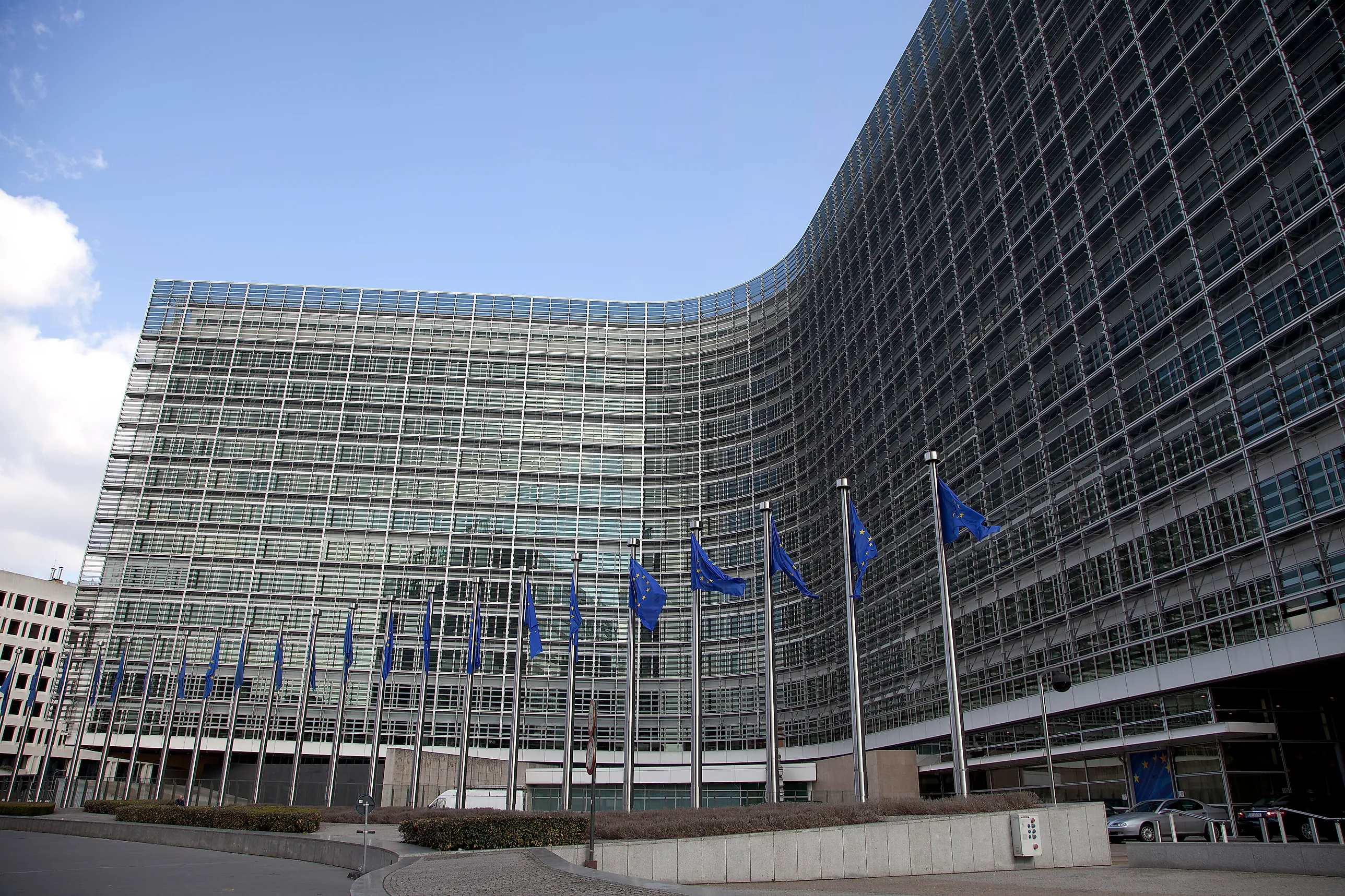Den böjda glasfasaden på Berlaymontbyggnaden i Bryssel med en rad EU-flaggor på stänger framför entrén.