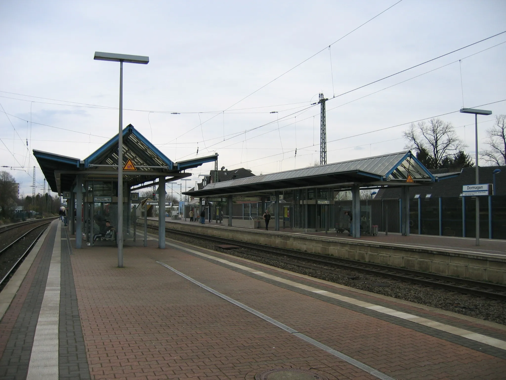 Tomma perronger med skärmtak vid en järnvägsstation, med en skylt där det står Dormagen.