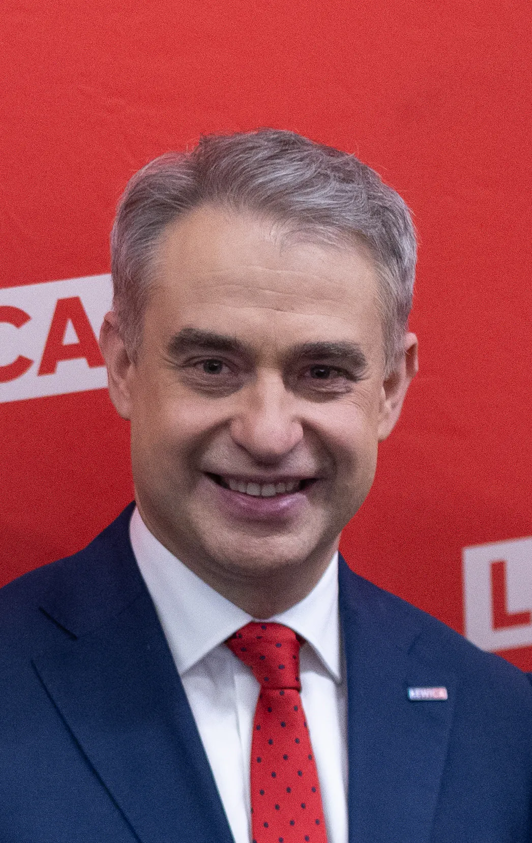 Krzysztof Gawkowski i mörkblå kavaj och röd slips framför en röd vägg.