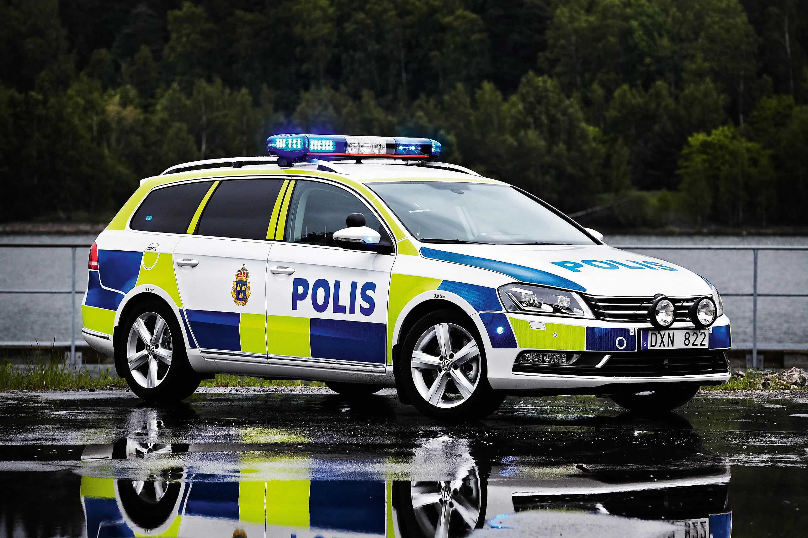 En vit polisbil med blå och gula rutor, blåljusramp på taket och texten POLIS på sidan.