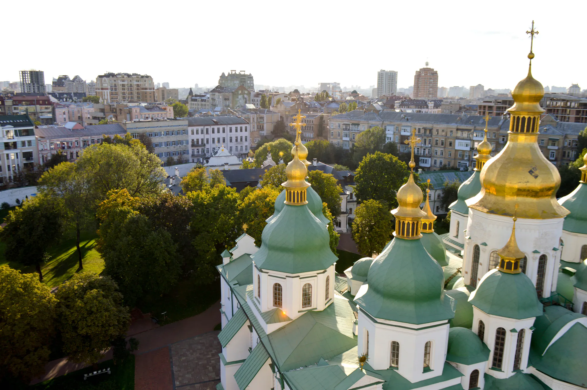 Gröna kupoler med förgyllda torn på Sofiakatedralen i Kyiv, med stadens hus och trädkronor i bakgrunden.