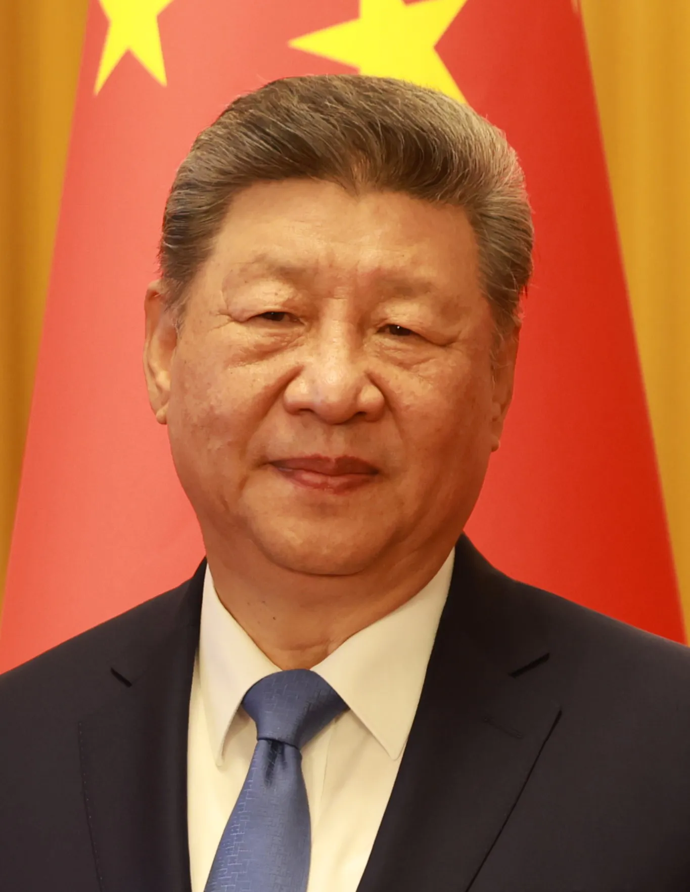 Xi Jinping i mörk kostym och blå slips framför en kinesisk flagga.