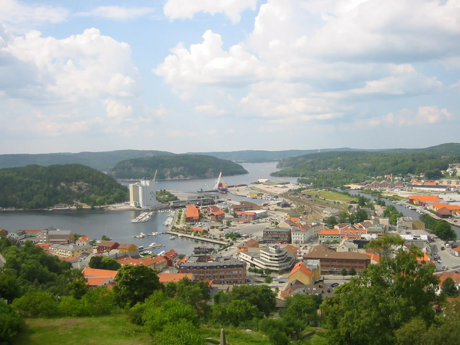 Vy över Haldens centrum med hamn, röda tegeltak och en fjord omgiven av skogsklädda höjder.