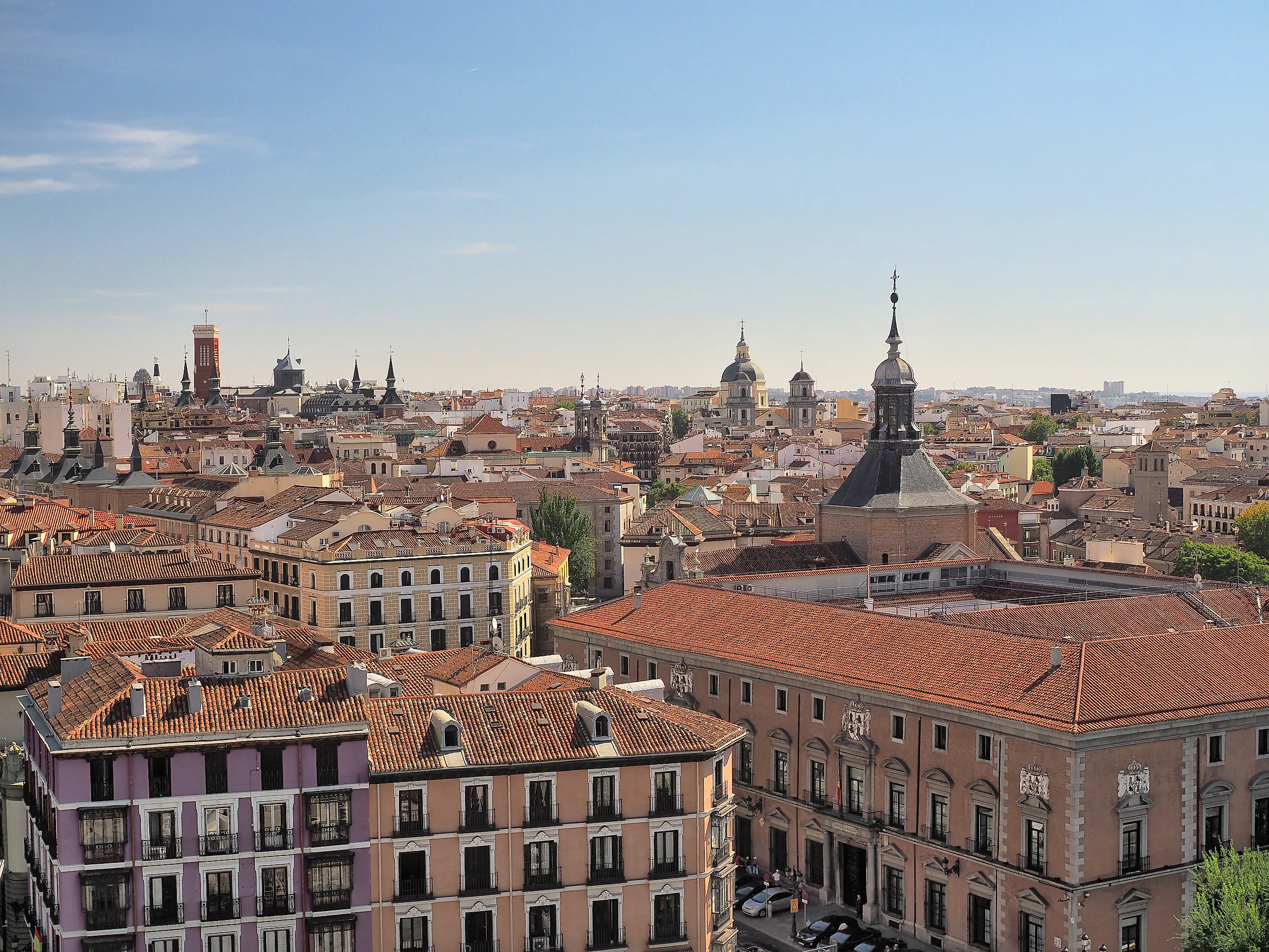 Tätt packade bostadshus med balkonger och tegeltak i centrala Madrid under blå himmel.